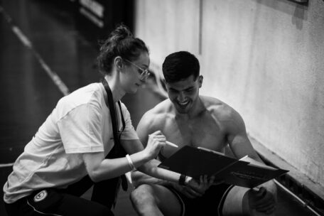 Keeping paperwork organized: Personal trainer reviews fitness plan with client on clipboard. Black and white image.