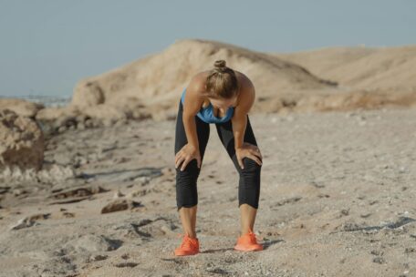 Exhausted woman resting after exercise in heat. Female runner with hands on knees, catching breath after workout.