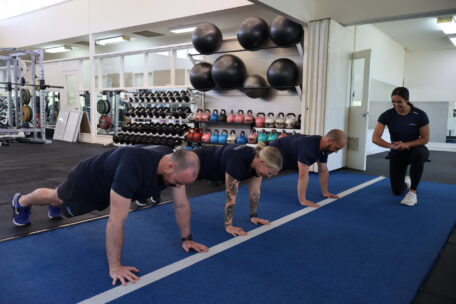 Gym instructor in Australia supervises a group doing push-ups. Fitness training for becoming a certified gym instructor.