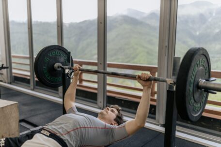 Man performing proper bench press technique with a barbell in a gym with mountain views to learn how to bench press.