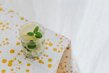 Hydration tips: Glass of infused water with lemon and mint on a yellow-spotted tablecloth. Stay hydrated for health and wellness.