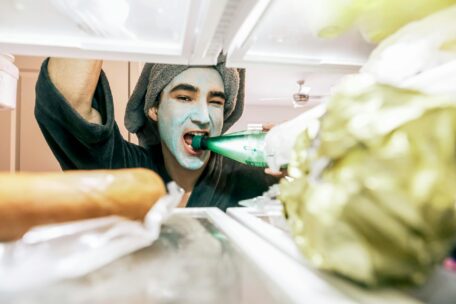 Staying Hydrated: Person with face mask drinking water from a bottle in the fridge. Tips on hydration and healthy lifestyle.