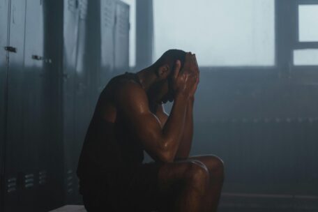 Overtraining: Sweaty athlete in locker room with head in hands, illustrating burnout and the importance of rest and recovery.