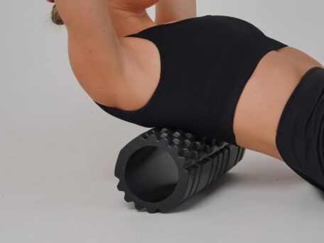 Woman using a black foam roller for muscle recovery. Foam roller exercises for back pain relief and improved flexibility.