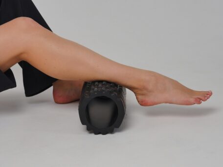 Woman using a foam roller on her lower leg, performing a recovery exercise for muscle relief and improved flexibility.
