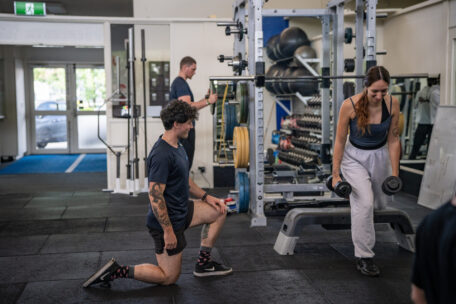 Personal trainer guiding woman lifting dumbbells in gym. Fitness training session. Weights and equipment visible.