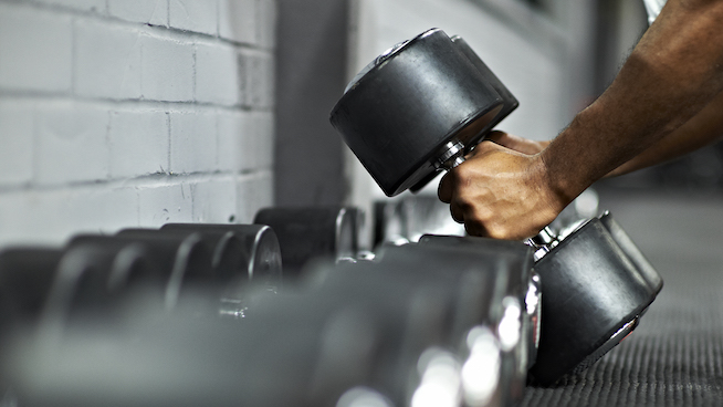 Strong black male picking up dumbbells from selection of free weights in gym, ready for workout