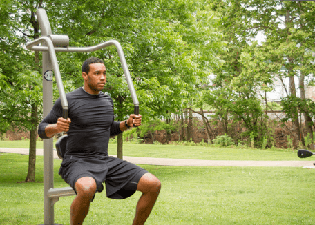 A young girl uses outdoor exercise equipment to exercise in a park