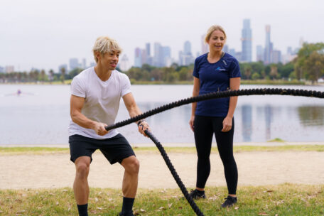 Personal trainer guiding a client using battle ropes outdoors to help build confidence and overcome imposter syndrome.