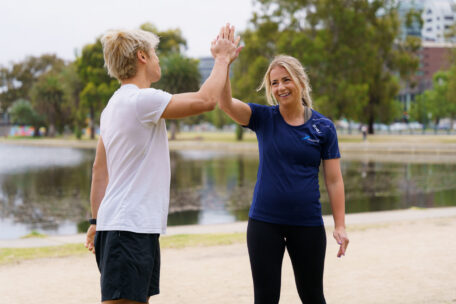 A personal trainer giving a high-five to a client outdoors to build confidence and overcome imposter syndrome.