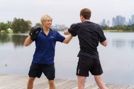 Personal trainer coaching a client with boxing pads outdoors, overcoming imposter syndrome through professional training.