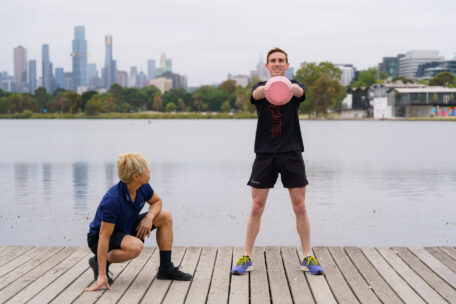 Personal trainer coaching a client with a kettlebell on a wooden pier with a city skyline view, overcoming imposter syndrome.